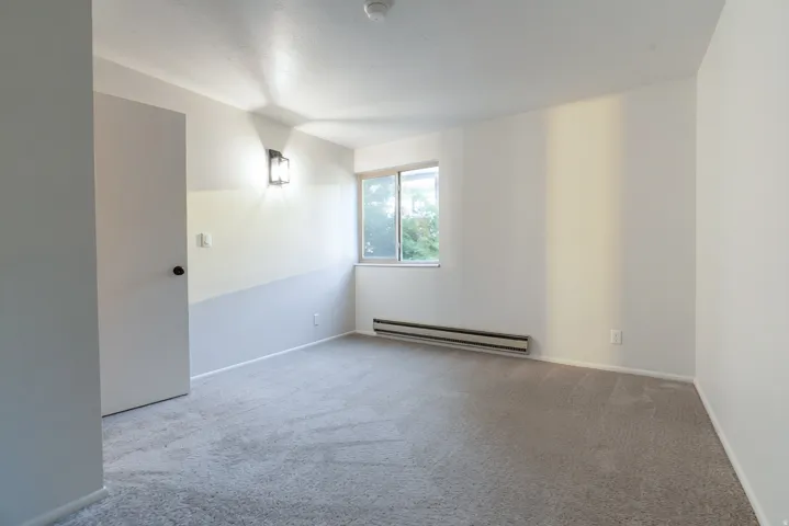 Neutral-toned carpeting, white painted walls, and a single window with white trim