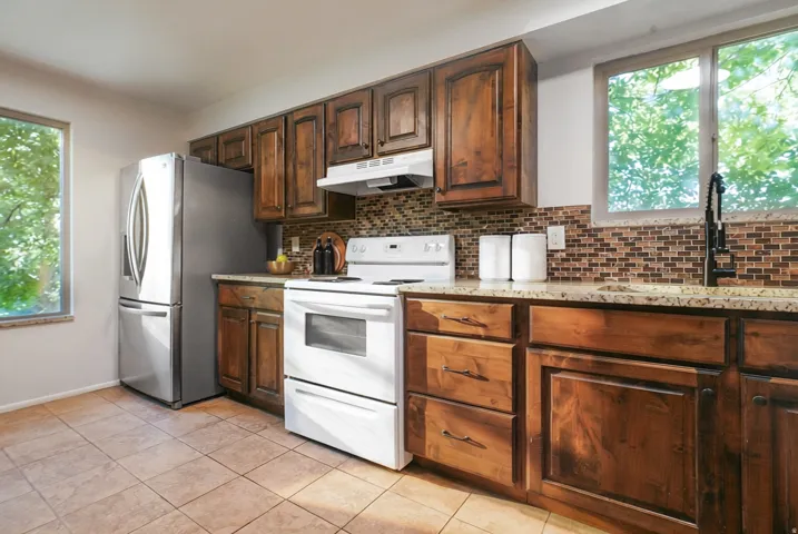 Kitchen featuring wood cabinetry, a mosaic tile backsplash, stone-finish countertops, and tile flooring