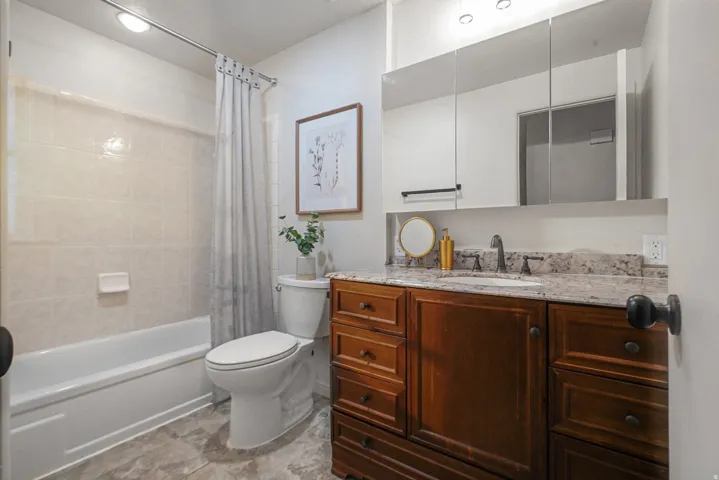 Wood-finish vanity with an integrated sink, granite countertop, and multiple mirror storage cabinets