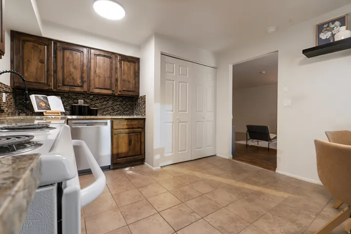 Kitchen featuring wood cabinetry, a mosaic tile backsplash, a built-in dishwasher, and tile flooring