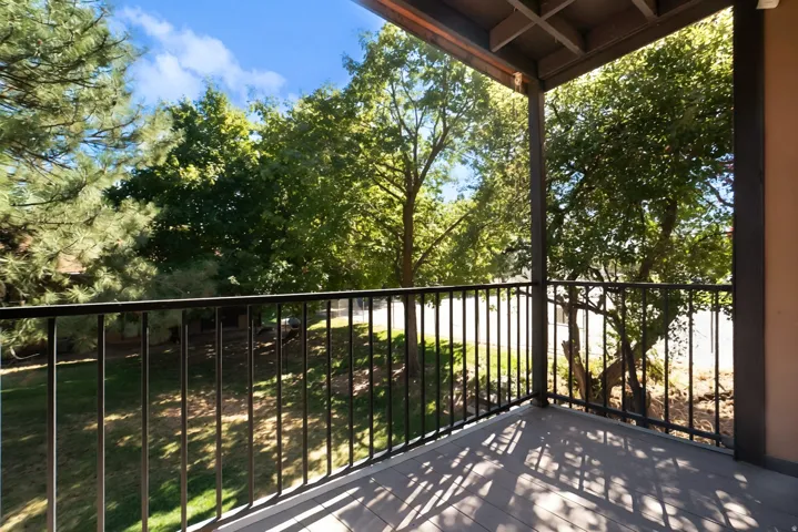 Covered deck with black metal railing overlooking mature landscaping and lush green lawn