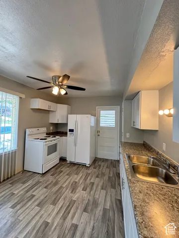Wood-finish flooring, white cabinetry, double basin stainless steel sink, ceiling fan with integrated lighting, and white appliances