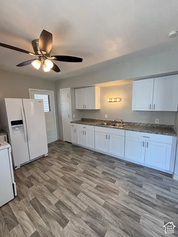 White shaker cabinetry, wood-finish flooring, dual basin stainless steel sink, ceiling fan with integrated lighting, and a built-in pantry cabinet