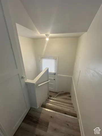 Stairwell featuring wood-finish flooring, white paneled walls, and a window with blinds