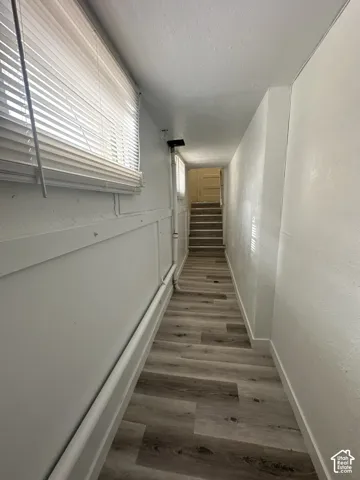 Wood-finish flooring extending into the stairwell, white wall paneling, and a single window with blinds