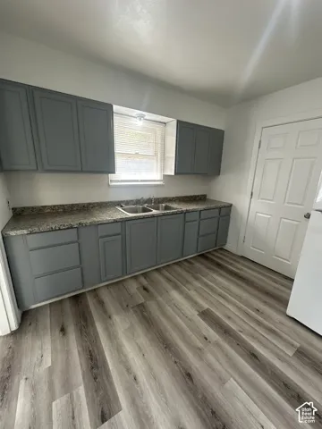 Gray cabinetry with a dual basin sink, speckled countertops, and wood-finish flooring