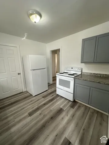 Wood-finish flooring, white refrigerator, white electric range, gray shaker-style cabinetry, and speckled countertop