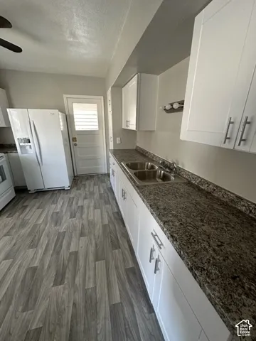 White cabinetry with brushed nickel hardware, speckled countertops, stainless steel double-basin sink, and wood-finish flooring