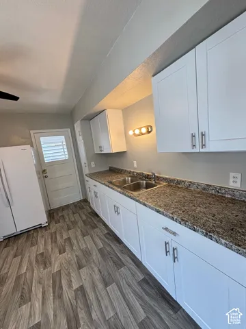 Kitchen featuring white cabinetry, speckled countertops, a double basin stainless steel sink, wood-finish flooring, and a ceiling fan