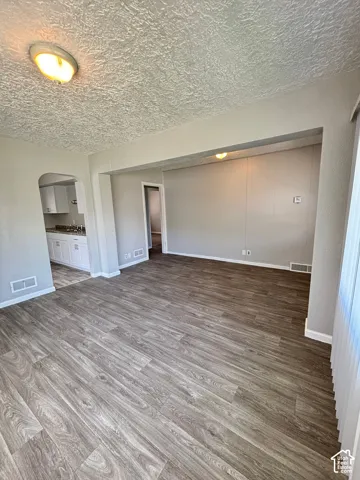 Spacious room with wood-finish flooring, light grey walls, and a recessed archway