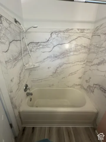 Bathtub with a handheld shower fixture, wall-mounted showerhead, and a marble-finish surround