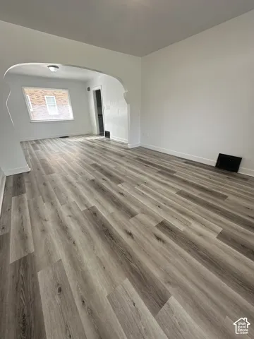 Wood-finish flooring, white wall paint, arched entry, window with brick exterior, and flush-mount ceiling light