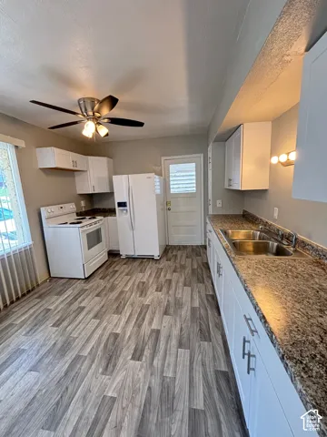 Kitchen featuring wood-finish flooring, white cabinetry, a dual-basin stainless steel sink, and a ceiling fan with integrated lighting