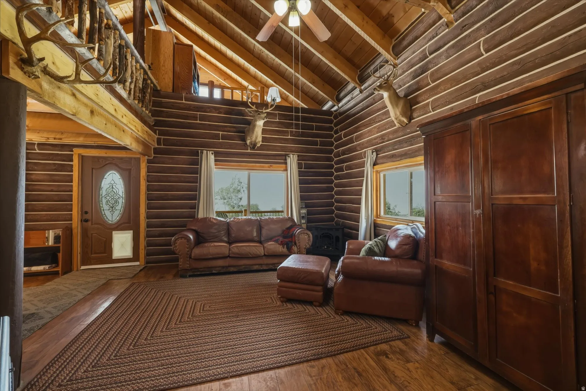 Vaulted wood-paneled ceiling with exposed beams, wood-finish flooring, log walls, and a decorative front door with an oval glass insert