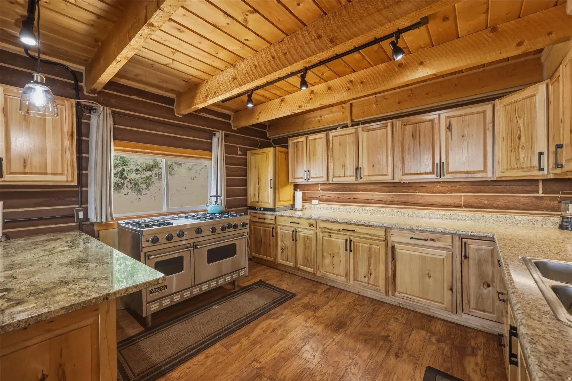 Wood-paneled walls and ceiling with exposed beams, wood-finish flooring, ample light wood cabinetry, and stainless steel range
