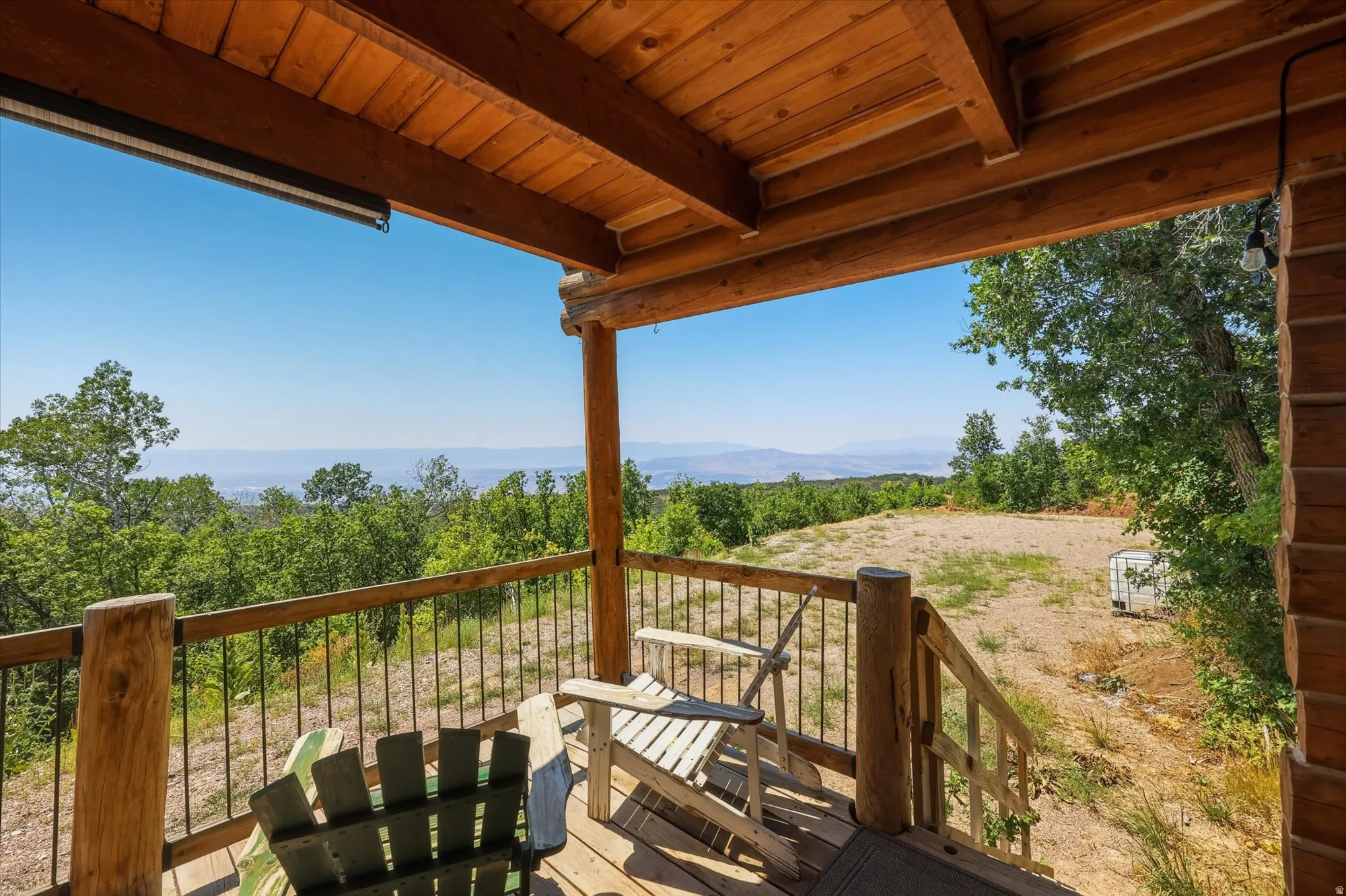 Covered wood deck with wood plank flooring, log-style support beams, and metal railing