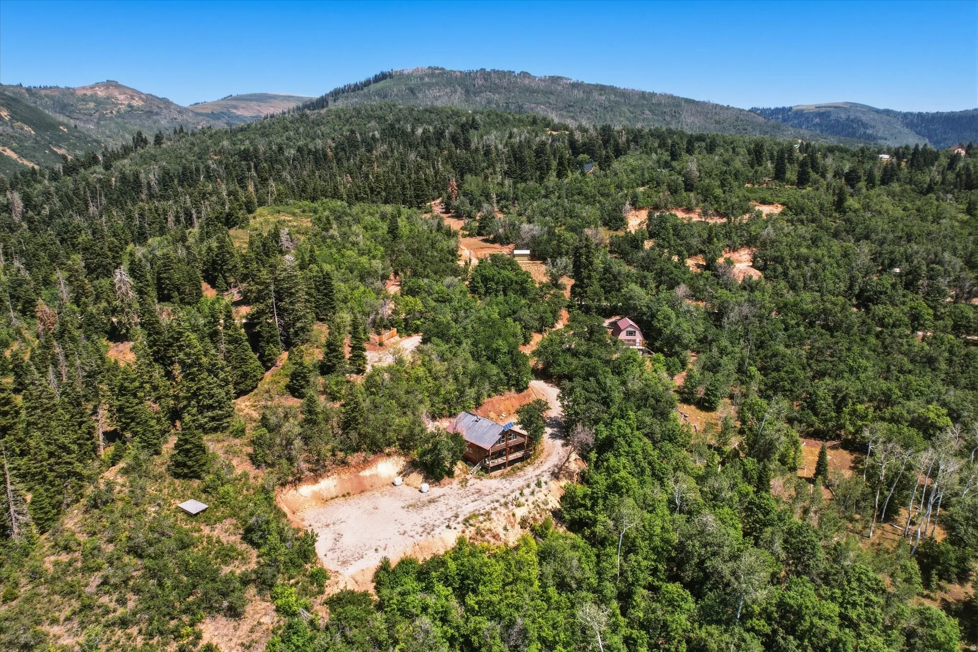 Expansive mountainous terrain with abundant trees, a distant peak, and multiple structures