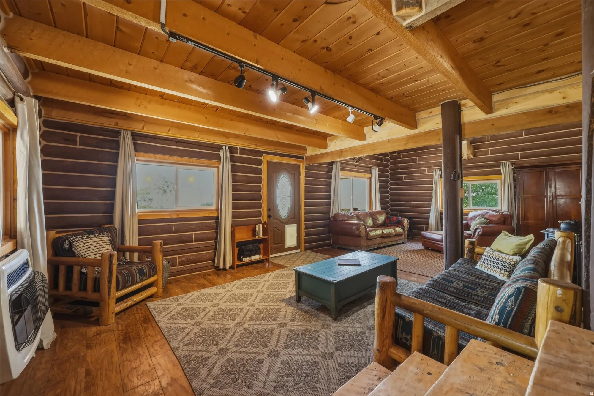 Wood-finish flooring, exposed wood beam ceiling, wood-paneled walls, built-in track lighting, and a decorative entry door