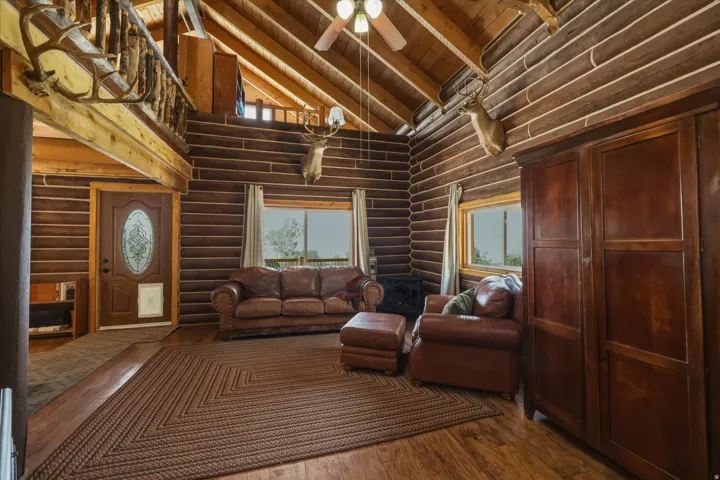 Vaulted wood-paneled ceiling with exposed beams, wood-finish flooring, log walls, and a decorative front door with an oval glass insert