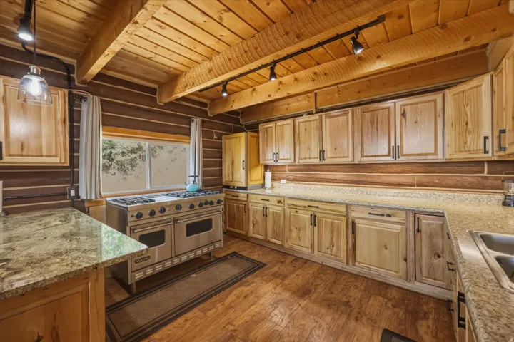 Wood-paneled walls and ceiling with exposed beams, wood-finish flooring, ample light wood cabinetry, and stainless steel range