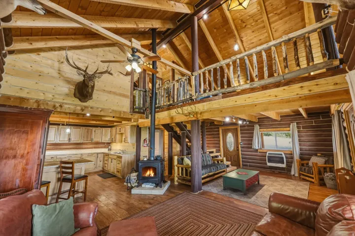 Vaulted wood-paneled ceilings, a functional wood-burning stove, open kitchen with wood cabinetry and countertop, and a lofted area with a wooden railing