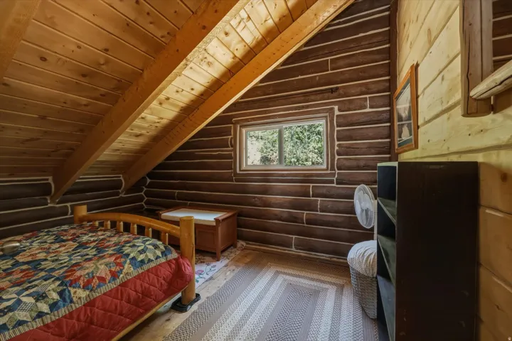 Attic space featuring log walls, an exposed beam ceiling, a window, and wood-finish flooring