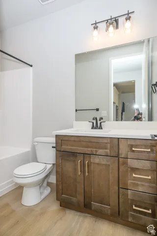 Wood-finish flooring, dark wood vanity with gold-tone hardware, white countertop with integrated sink, black-finish faucet, and a wall-mounted light fixture