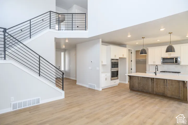 Open-concept layout featuring wood-finish flooring, a modern kitchen island with pendant lighting, white cabinetry, and stainless steel double ovens