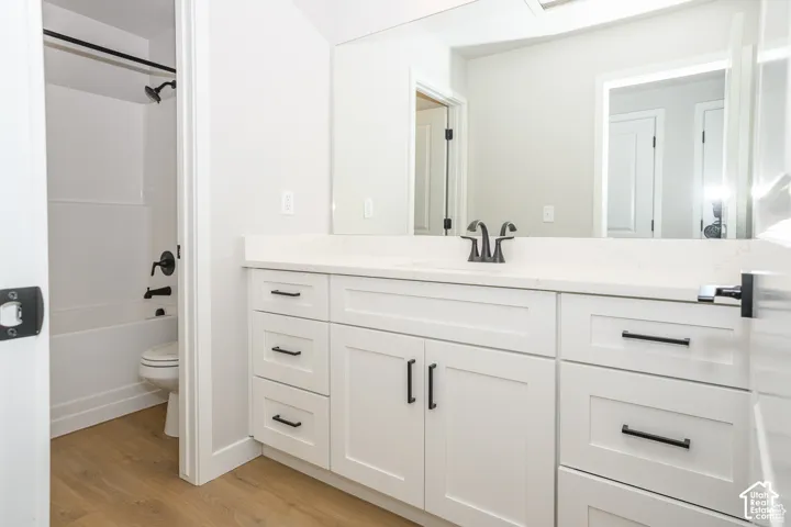 White shaker-style cabinetry with matte black hardware, light-toned countertop, rectangular undermount sink with matte black faucet, and wood-finish flooring