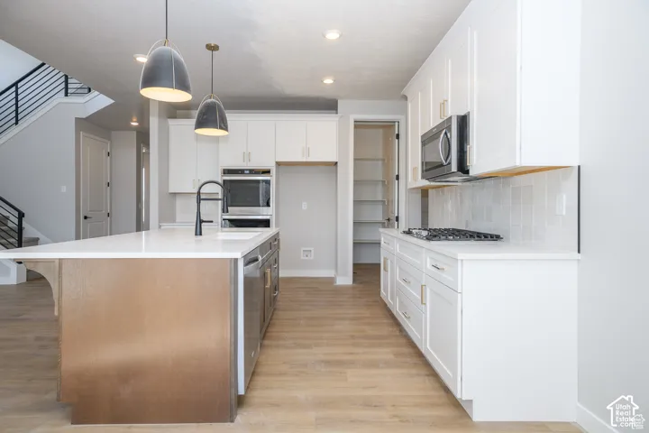 Modern kitchen featuring white cabinetry, a wood-finish island with a white countertop, stainless steel appliances, and wood-finish flooring