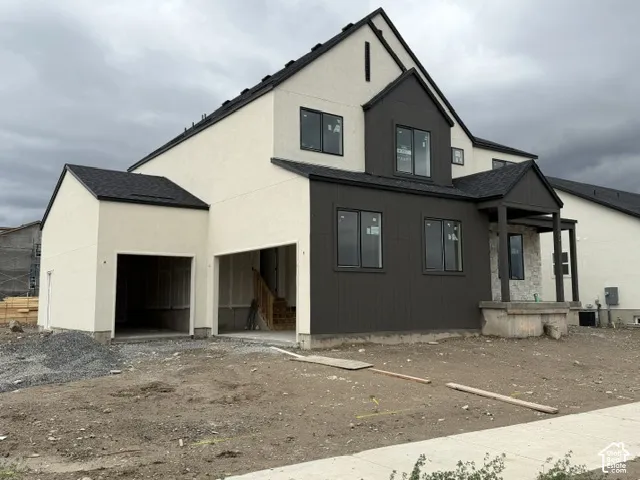 Two-story exterior featuring a textured stucco finish, board-and-batten siding, asphalt shingle roof, stone masonry accents, and an attached multi-car garage