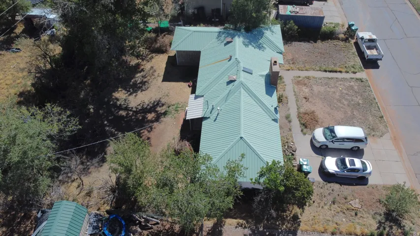 Green metal roof with a chimney, a detached structure with a matching green metal roof, and an adjacent unpaved area