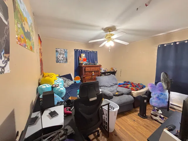 Hardwood flooring, ceiling fan, and window with dark drapes