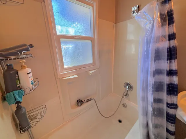 Bathtub with integrated shower, chrome fixtures, and a privacy window