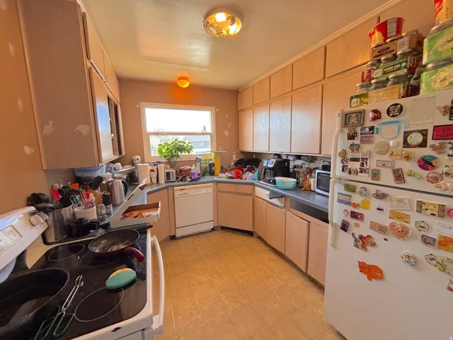 Galley-style kitchen featuring wood-finish cabinetry, cork flooring, and stainless steel appliances