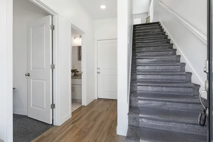 Wood-finish flooring in the entryway, white paneled doors, and a staircase with carpeted treads