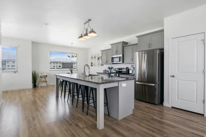 Open-concept kitchen featuring an oversized island with seating, stainless steel appliances, gray shaker-style cabinetry, a granite countertop, and wood-finish flooring