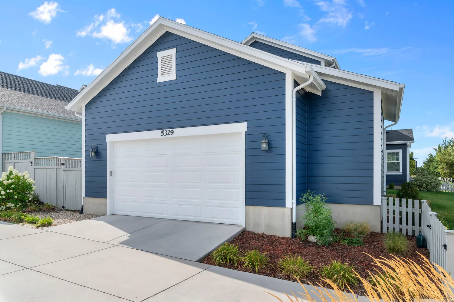 Attached two-car garage with white paneled door, blue horizontal siding, and white trim accents