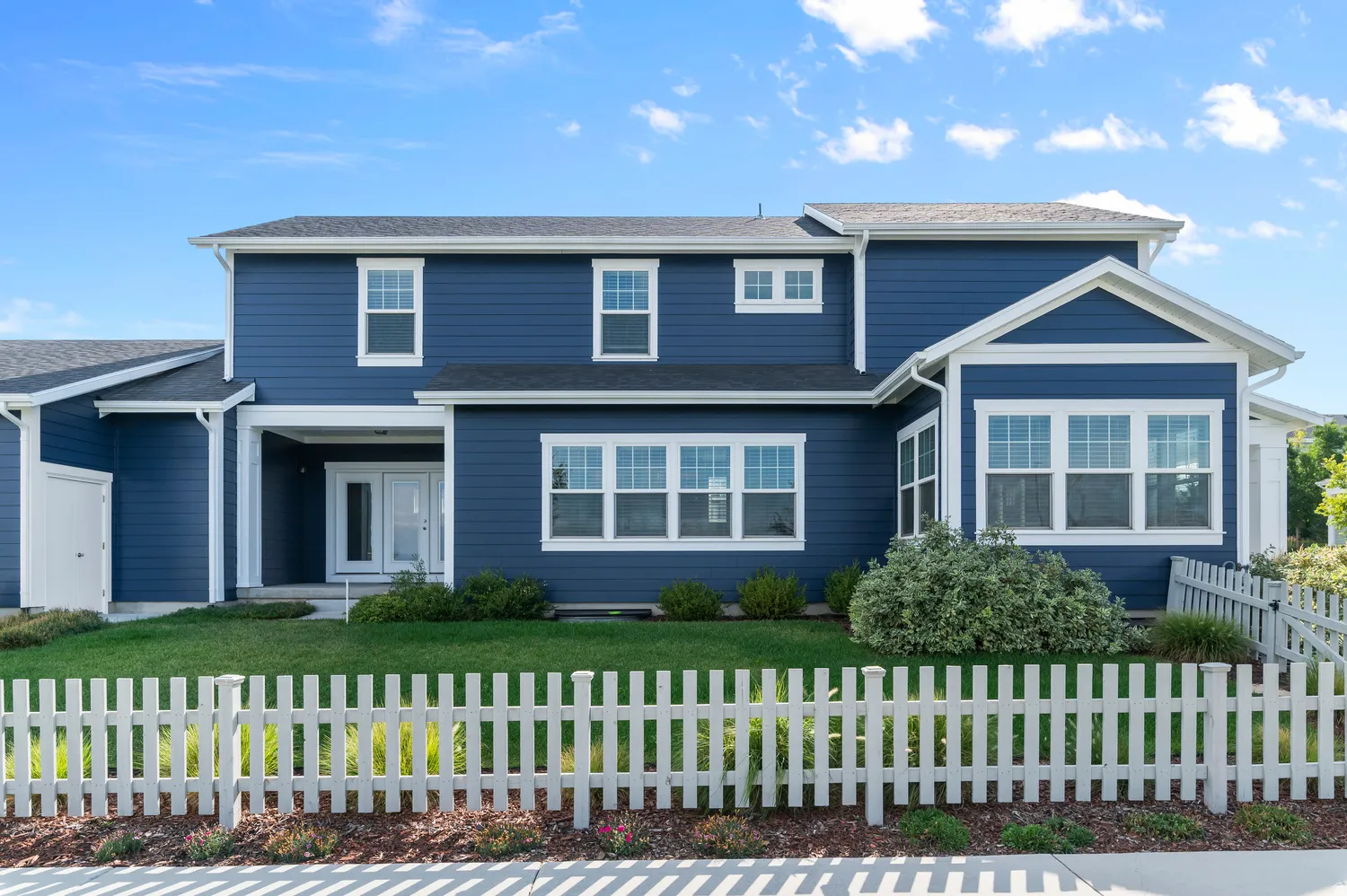 Blue siding exterior with white trim, a covered entry, multiple white-framed windows, and a white picket fence