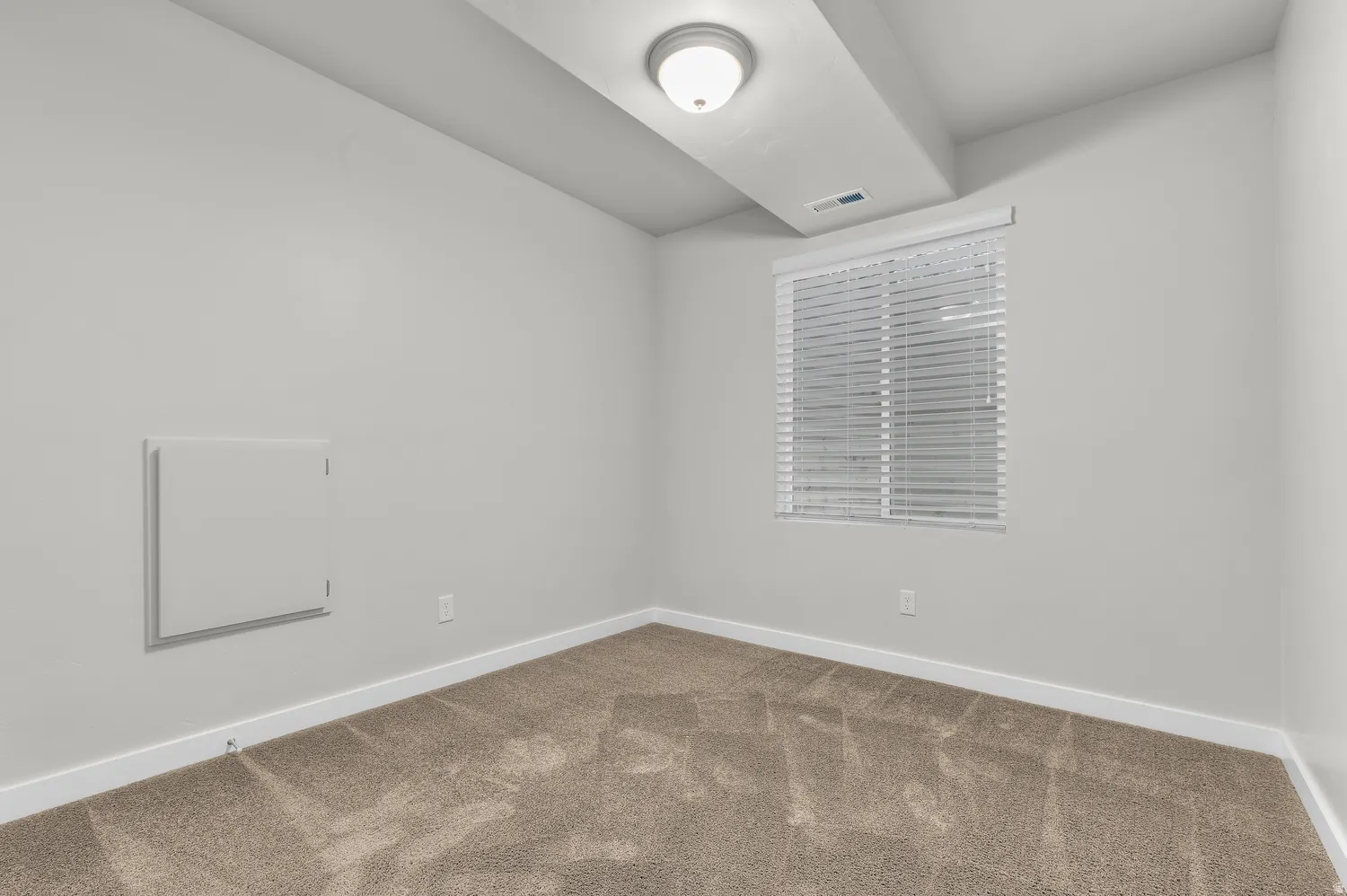 Neutral wall paint, textured carpeting, a window with horizontal blinds, and overhead lighting