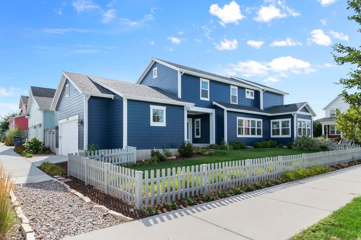 Two-story residence featuring blue siding, white trim, a white picket fence, a two-car garage, and a front lawn