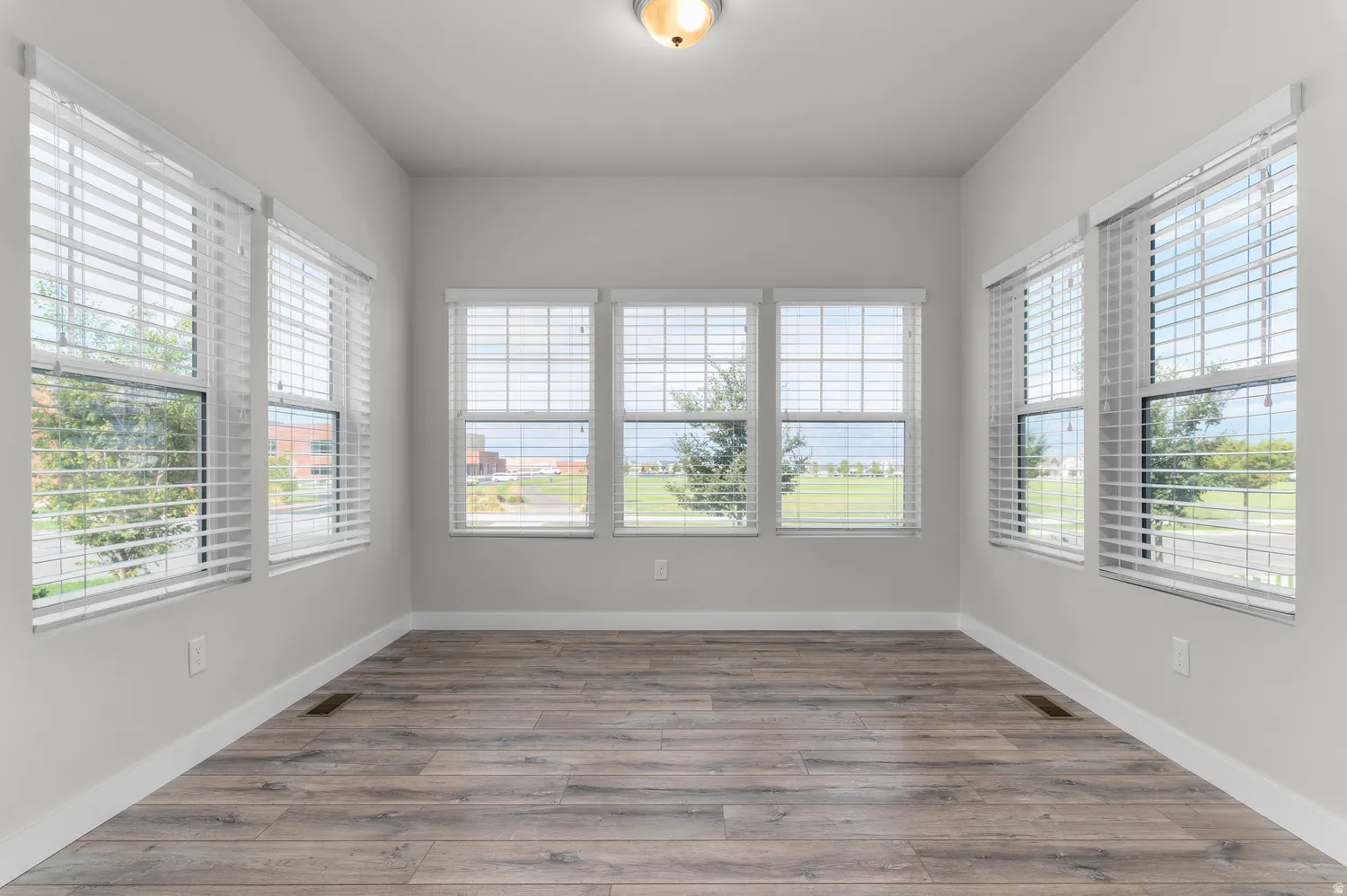 Wood-finish flooring, multiple windows with blinds, and white trim