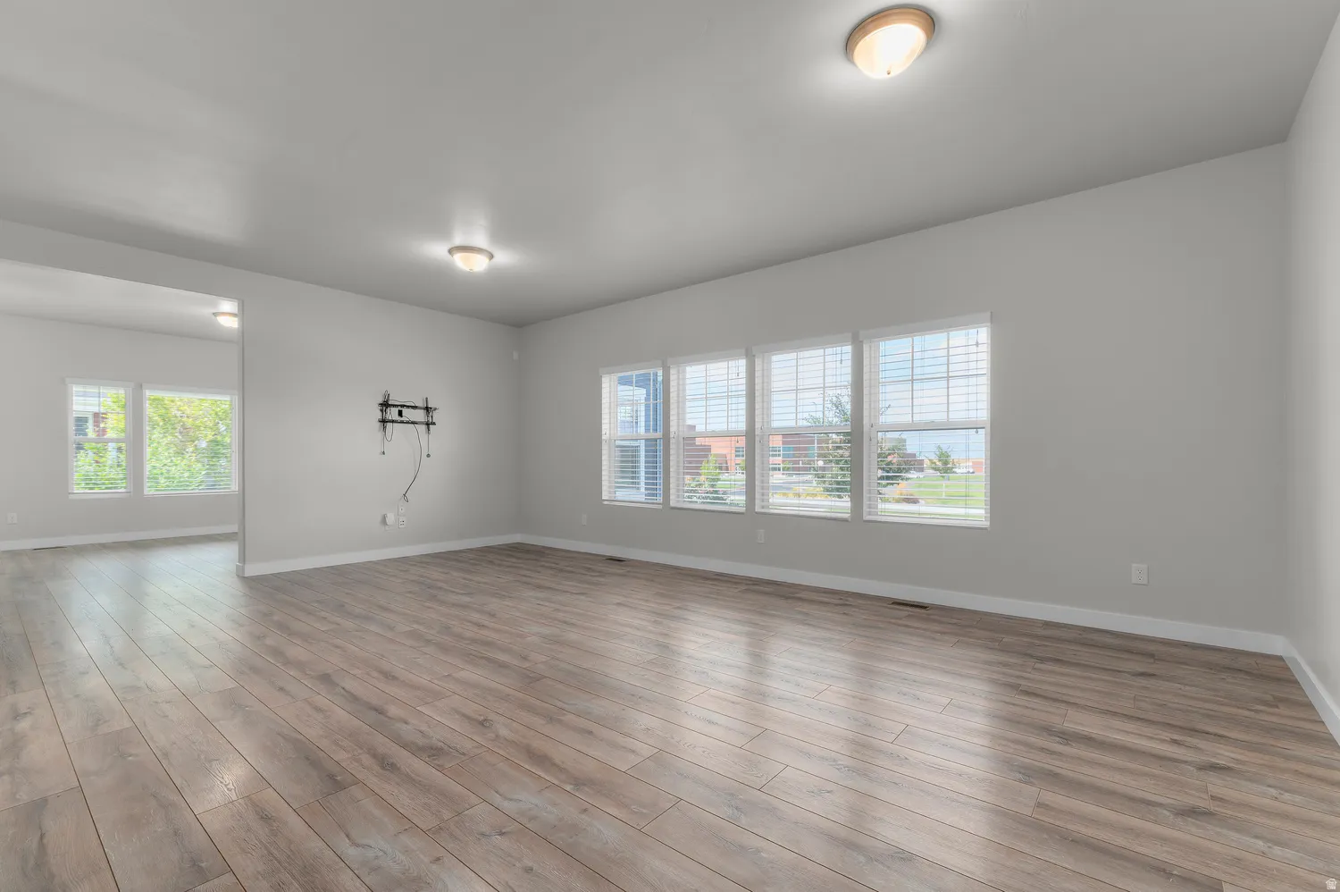 Expansive room featuring wood-finish flooring, light gray wall tones, multiple windows with blinds, and flush-mount ceiling lights