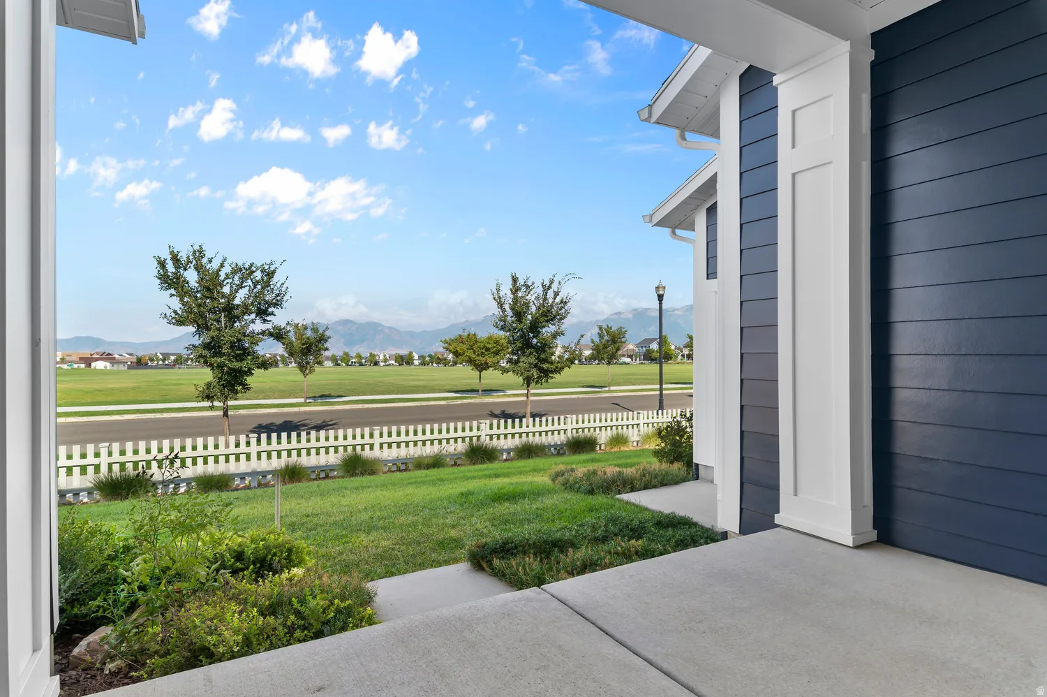 Covered concrete patio with a white pillar, blue horizontal siding, and a white picket fence