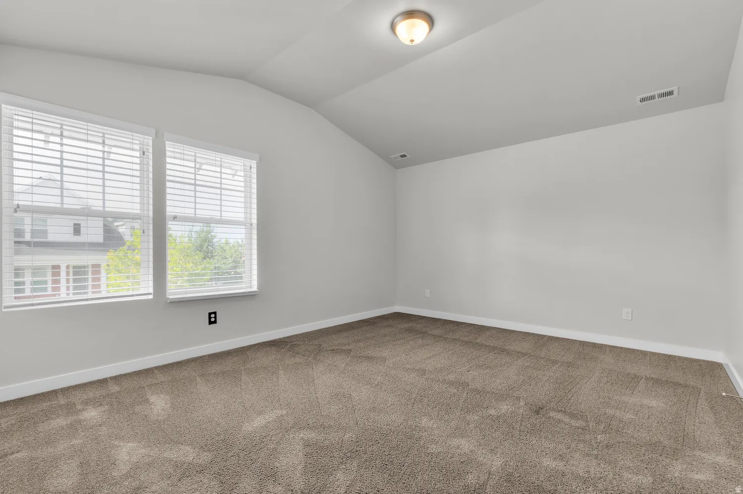 Neutral wall color, vaulted ceiling, two windows with blinds, and carpeted flooring