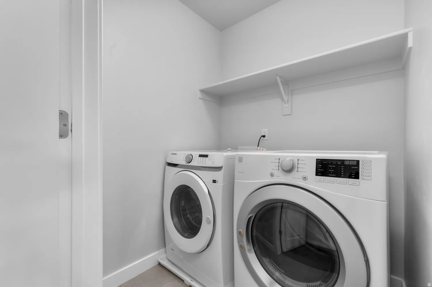 Dedicated laundry area featuring a wall-mounted white shelf, light-toned wall paint, and light-colored flooring