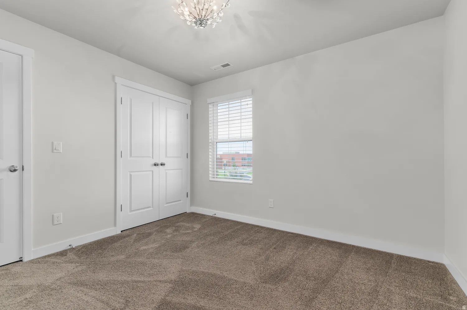 Neutral wall paint, plush carpet flooring, a multi-pane window with blinds, and a built-in double-door closet