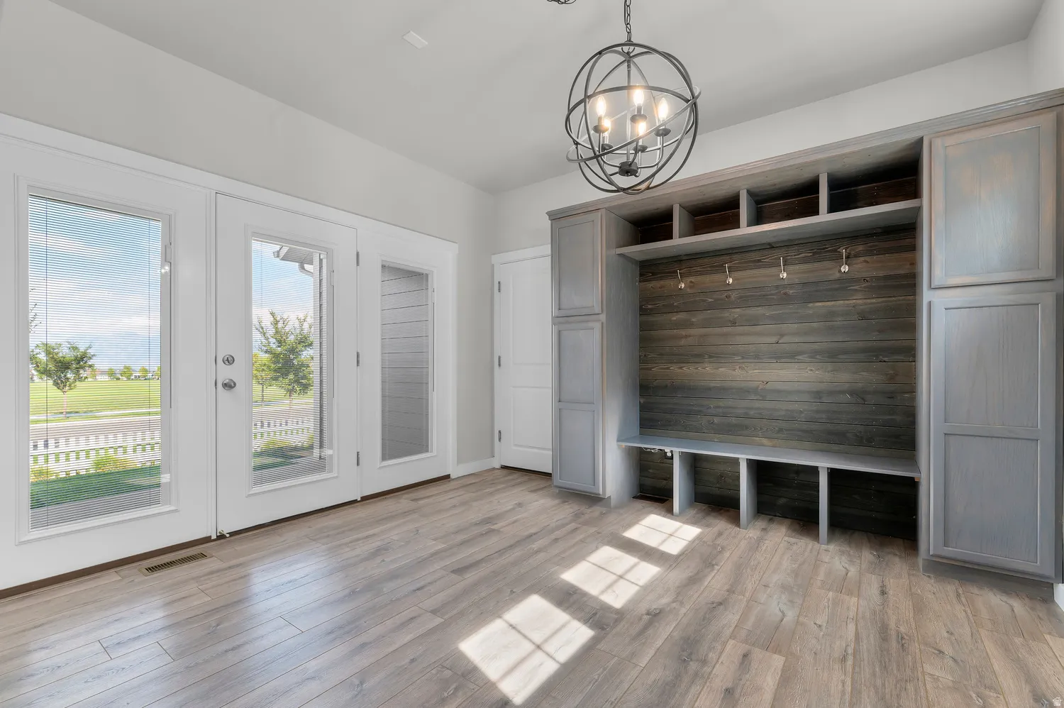 Wood-finish flooring, built-in storage with shaker-style cabinetry, integrated bench seating, and an overhead spherical chandelier