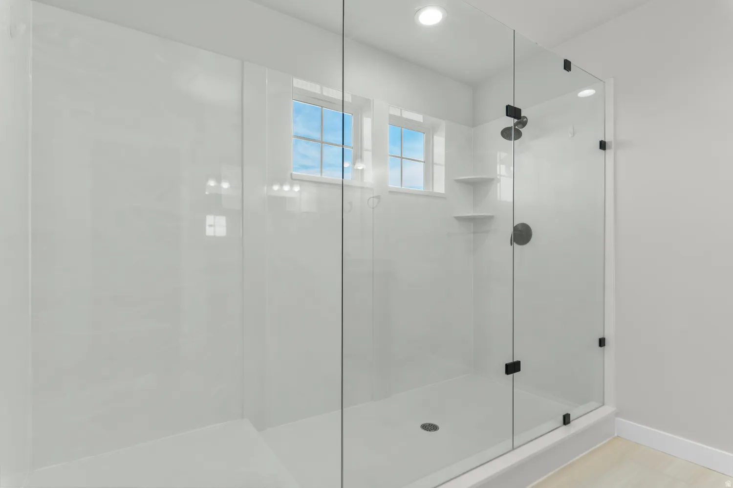 Glass-enclosed shower with white paneling and a matte black shower fixture