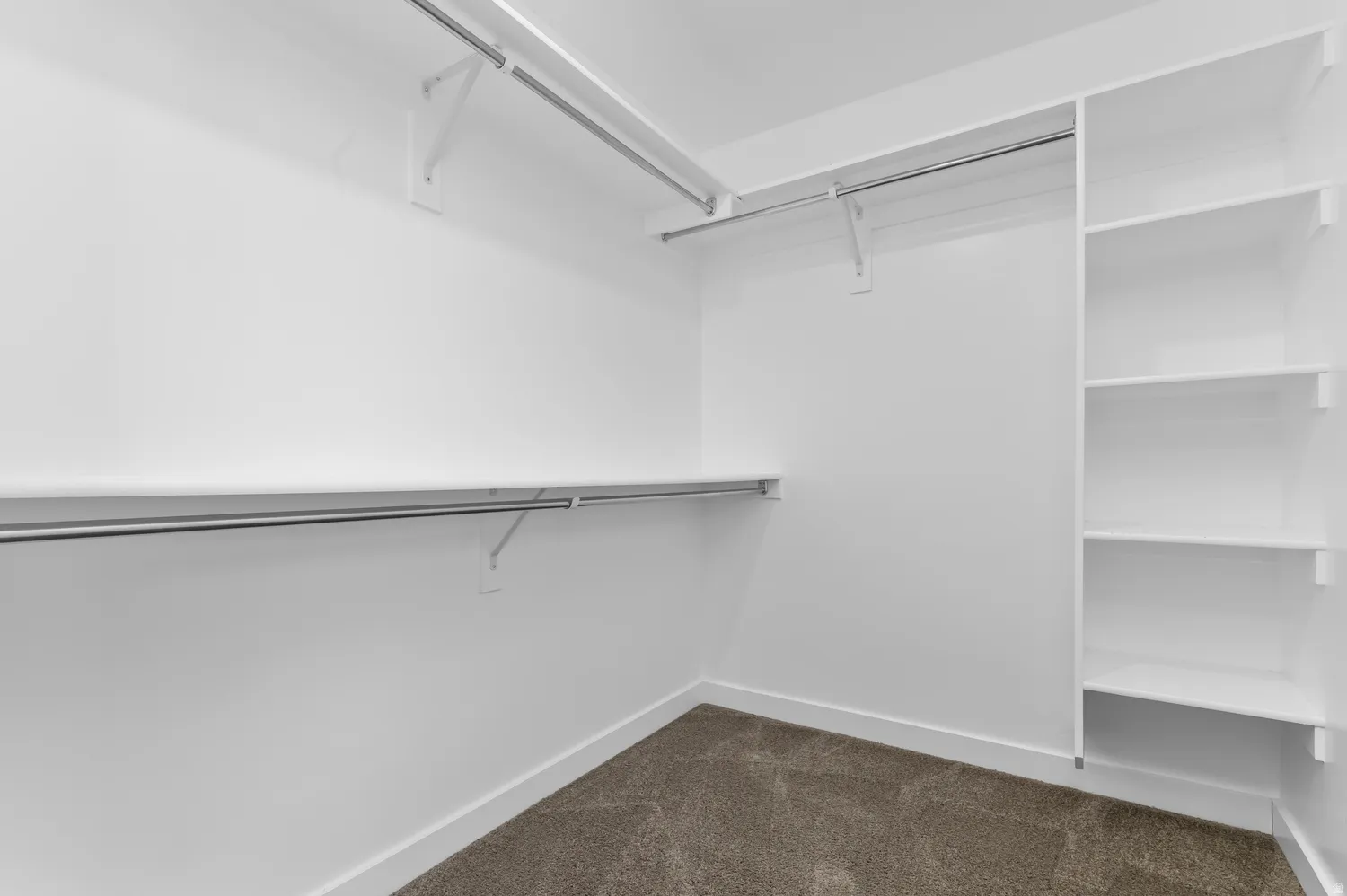 White shelving unit, multiple hanging rods, and dark carpeting